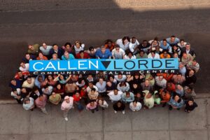 Staff standing around a Callen-Lorde flag and looking up at the camera.